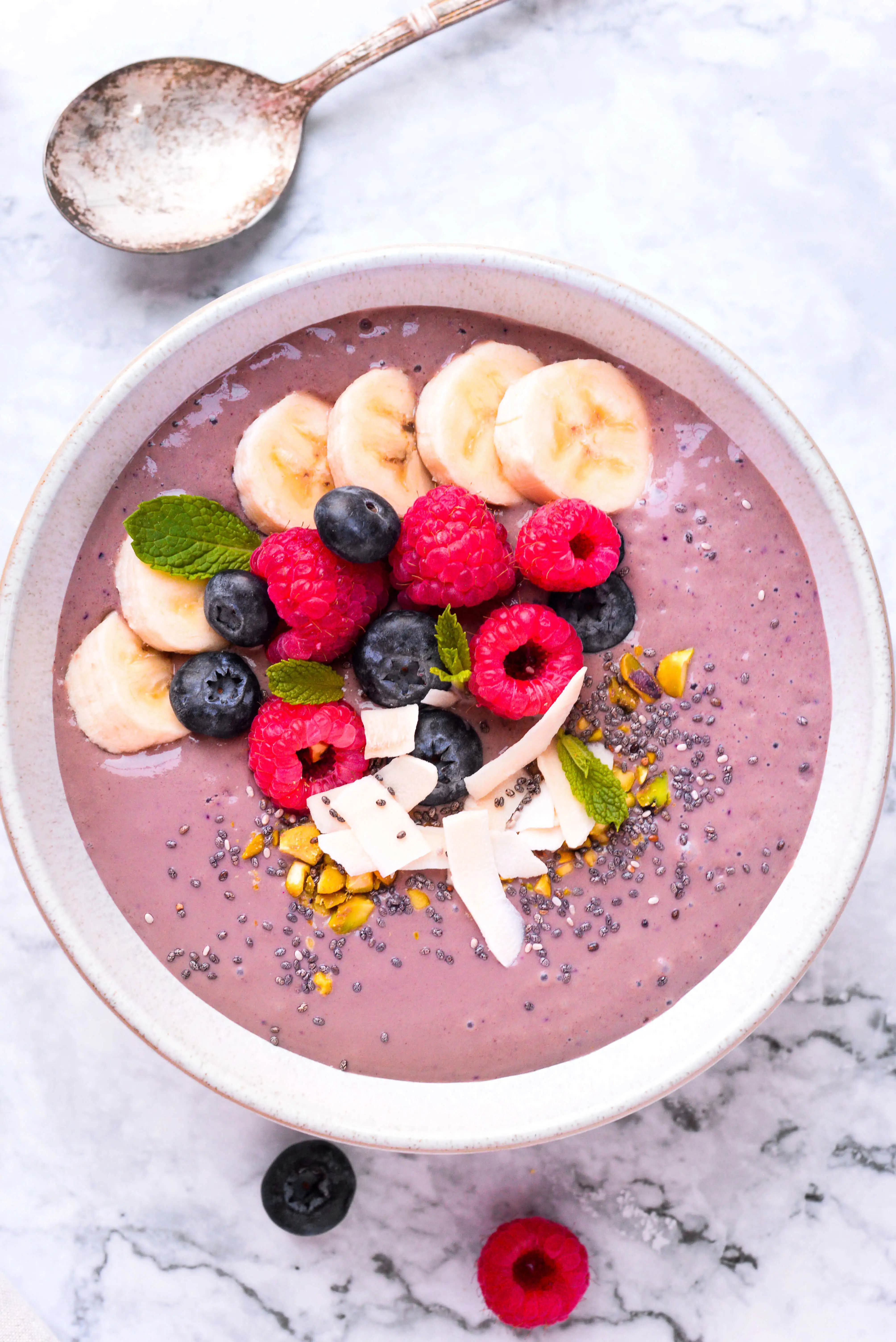 紫色的阿卡伊碗上面放着浆果,奇亚种子,椰子片,开心果和薄荷。